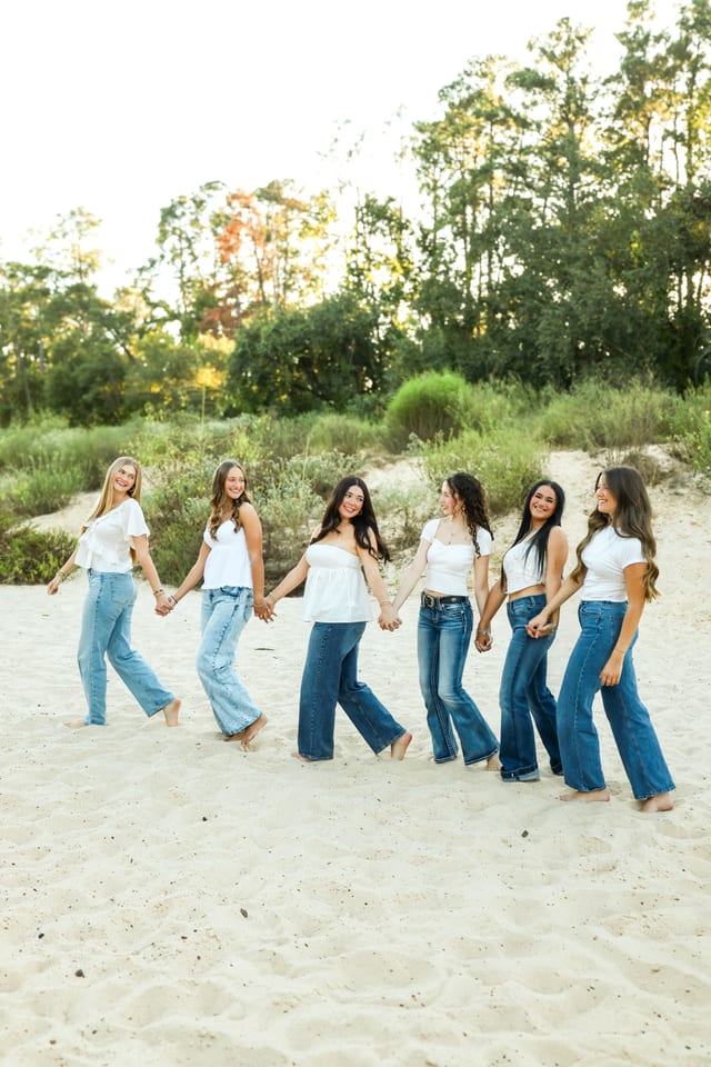 Group of friends in white tops and denim on a sandy beach
