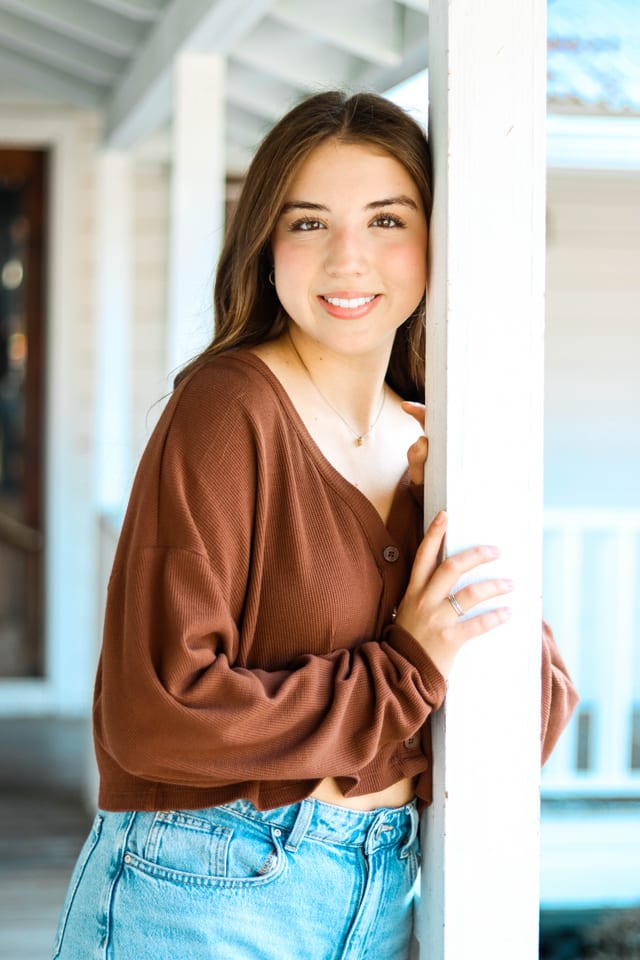 Senior in a brown sweater on a white porch