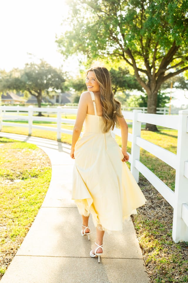 Senior in a pale yellow dress beside a white fence