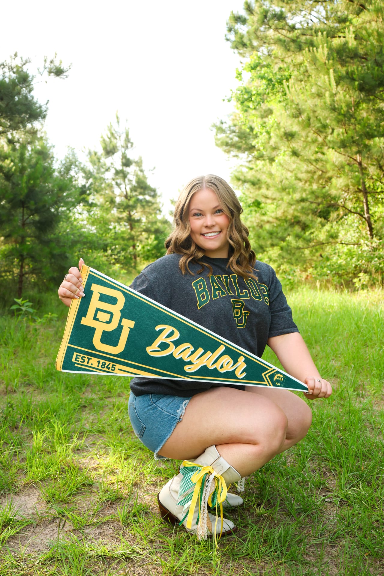 Senior holding a Baylor pennant in the woods