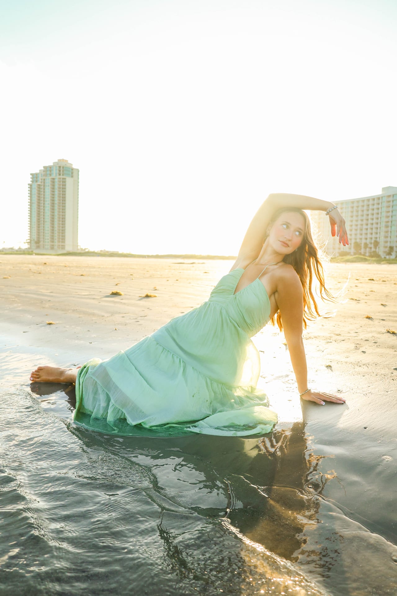 Senior in mint dress sitting in shallow surf at the beach