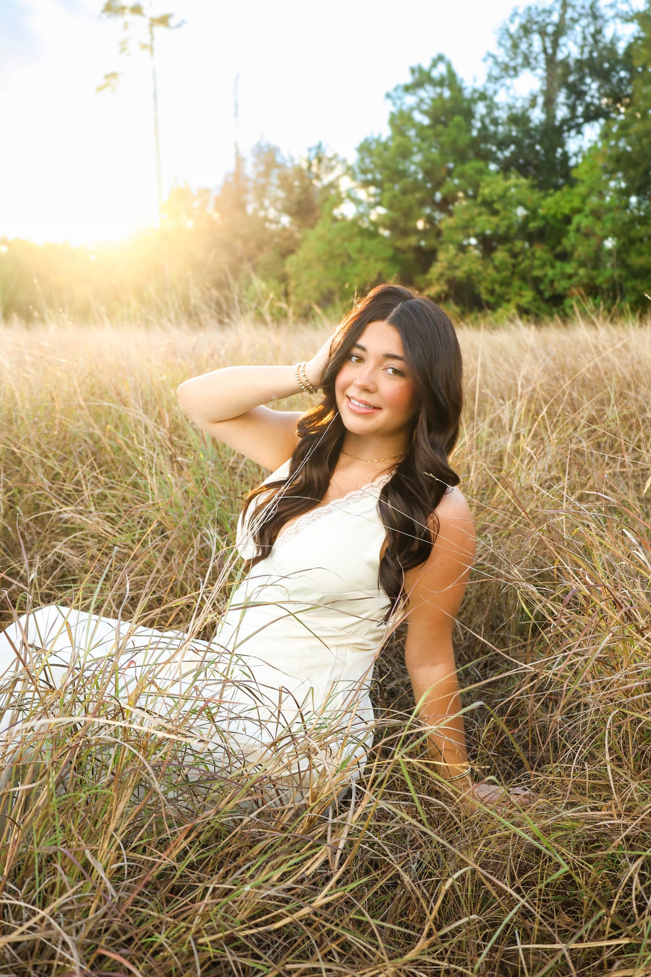 Senior in white dress sitting in tall golden grass