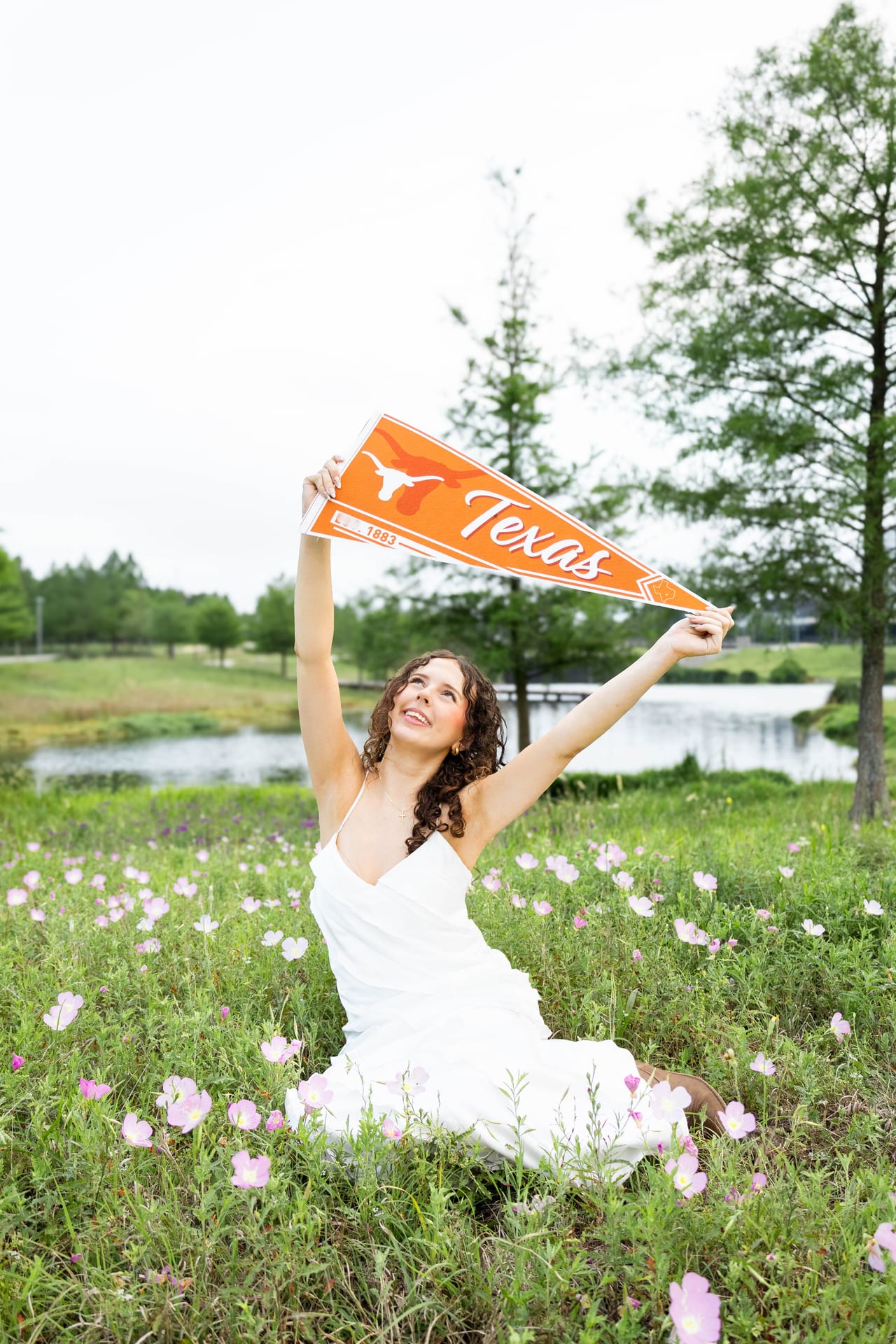 Senior holding a Texas pennant in a field of pink wildflowers