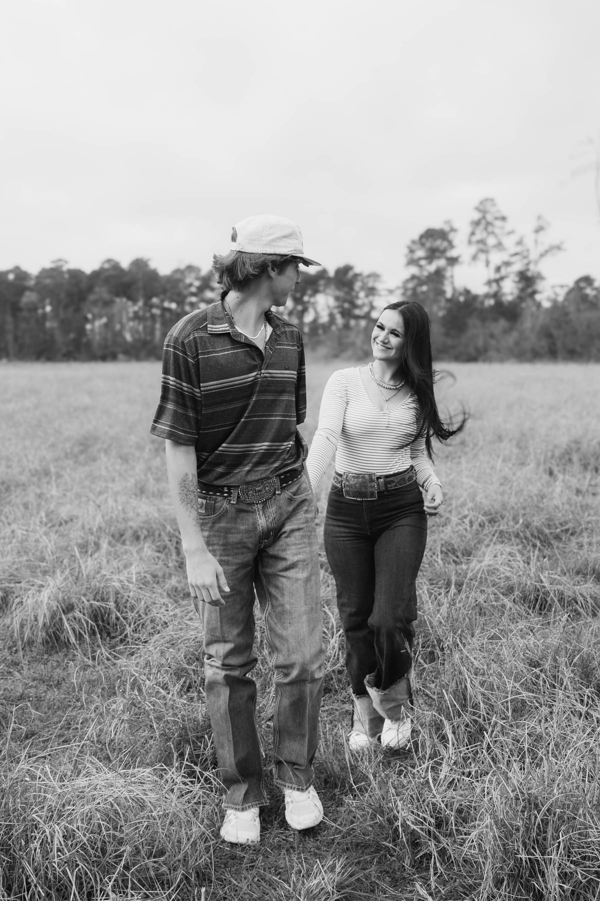 Black and white candid of a couple walking hand in hand through a field