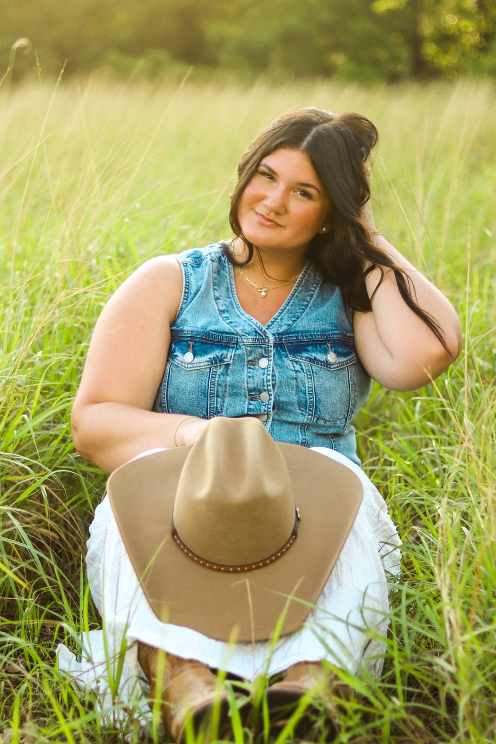 Senior in denim vest and cowboy hat in a grass field